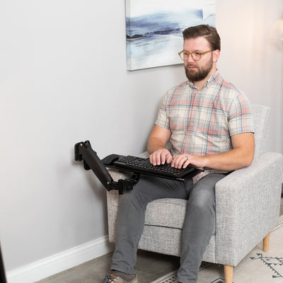 Man typing from a comfortable chair in a modern office space.